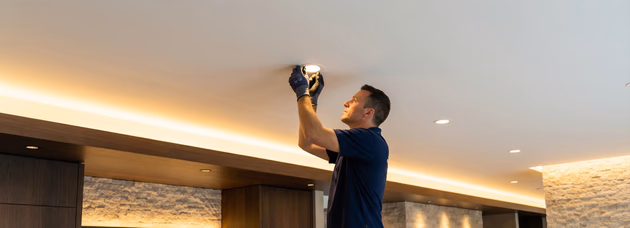 Electrician completes wiring in a renovated room with exposed studs and tools nearby.