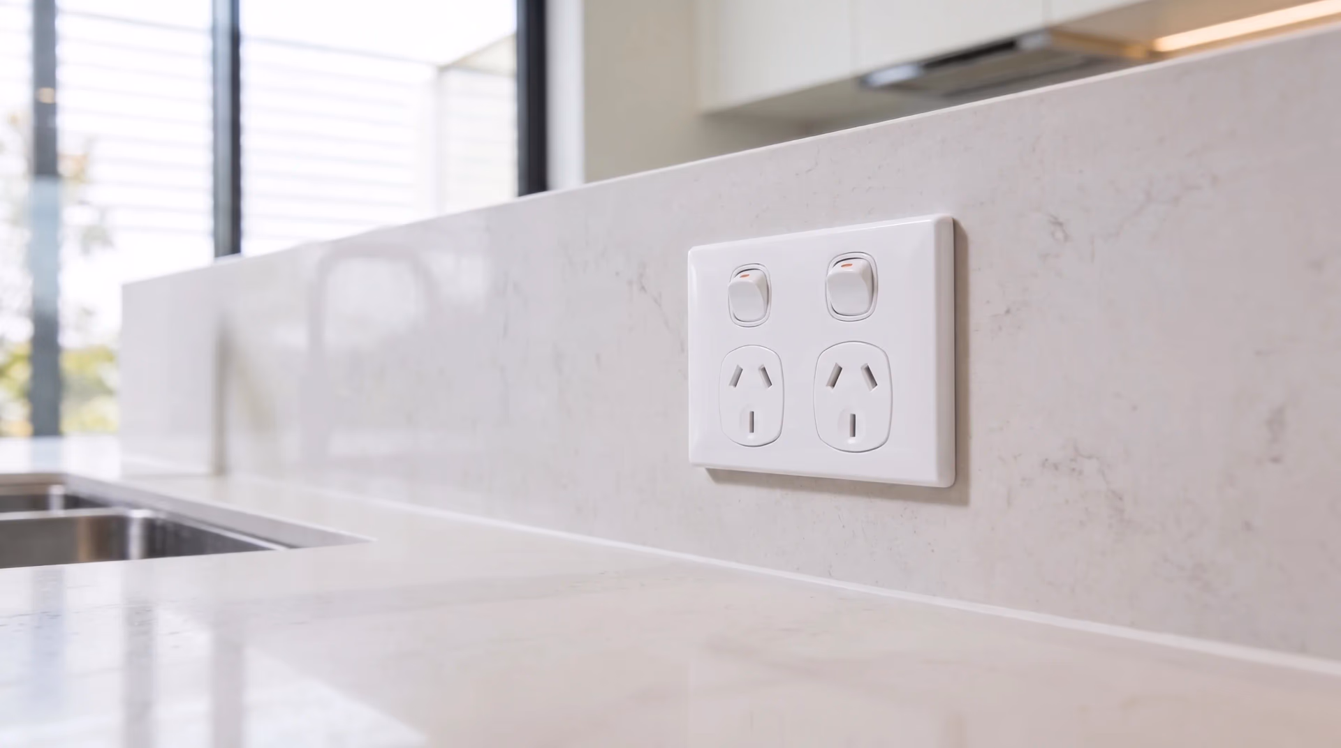 A white double power point mounted on the stone splashback of a new kitchen.
