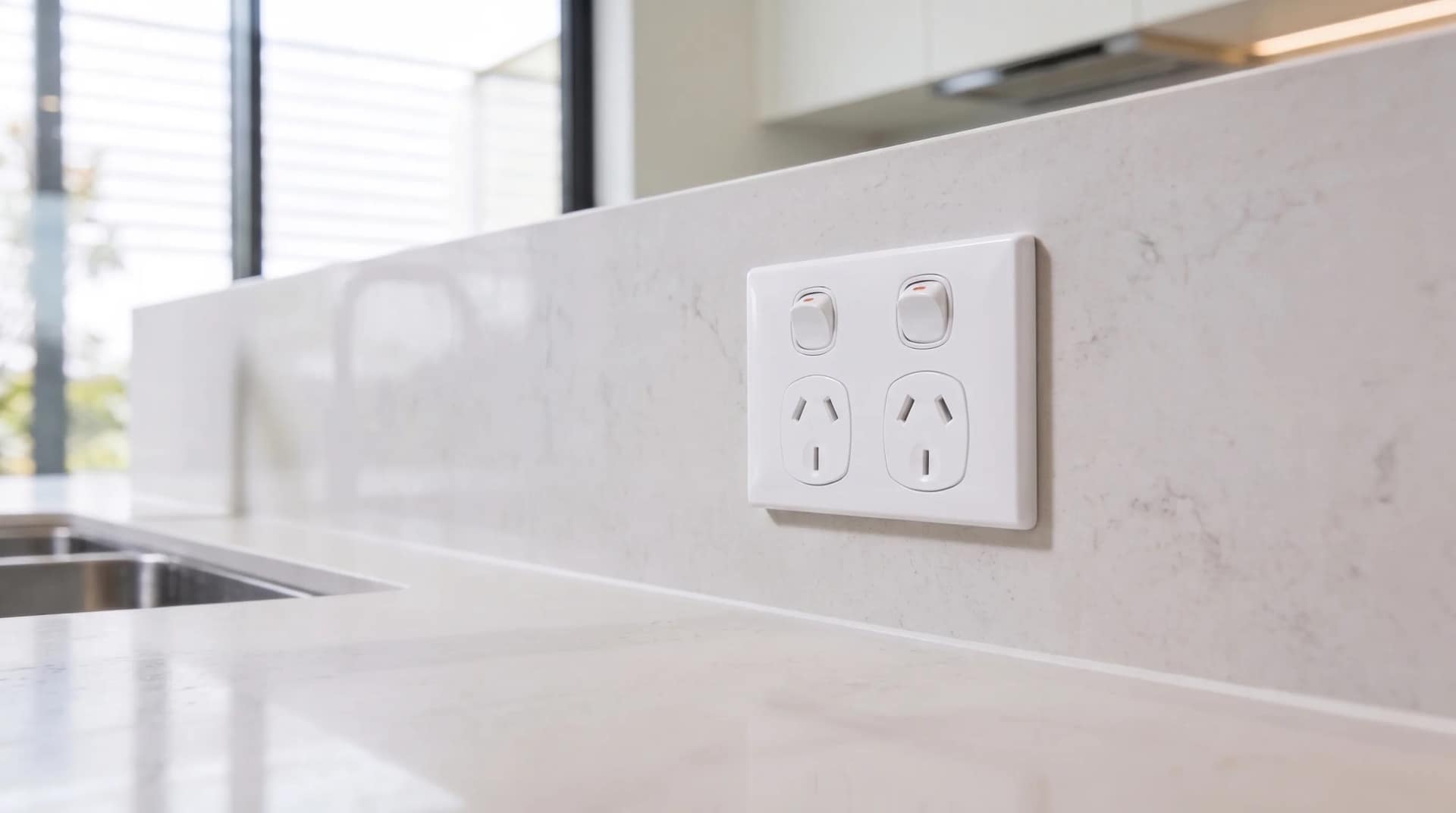 A white double power point mounted on the stone splashback of a new kitchen.